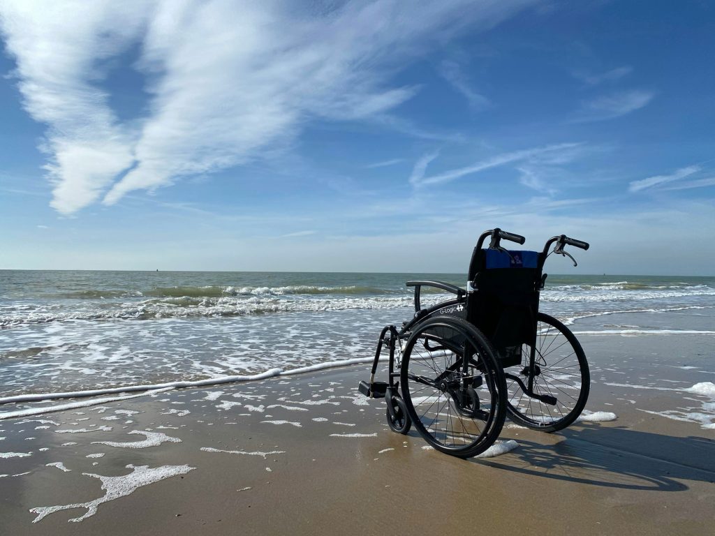 Empty wheelchair on a beautiful beach, facing the ocean.